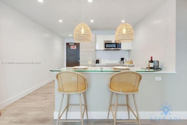 kitchen with white cabinets, a breakfast bar, pendant lighting, and light hardwood / wood-style flooring