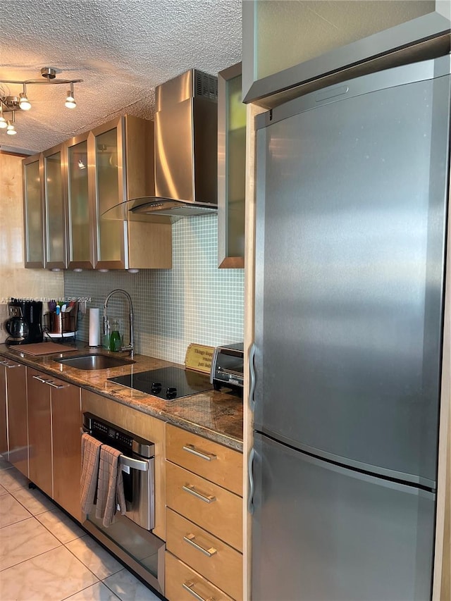 kitchen featuring sink, wall chimney exhaust hood, stainless steel appliances, dark stone countertops, and a textured ceiling