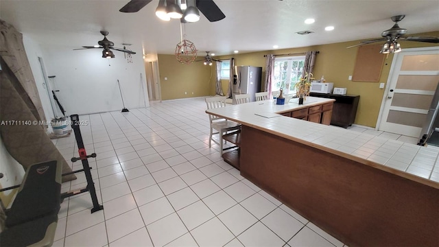 kitchen with decorative light fixtures, tile counters, light tile patterned flooring, stainless steel fridge with ice dispenser, and a breakfast bar area