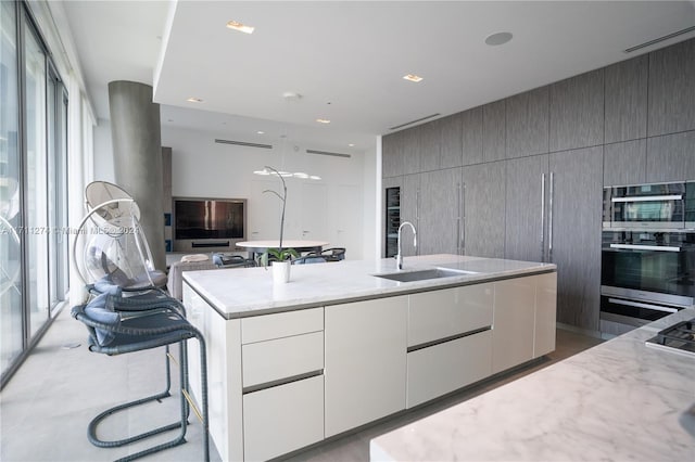 kitchen featuring a breakfast bar, a large island with sink, sink, double oven, and white cabinetry