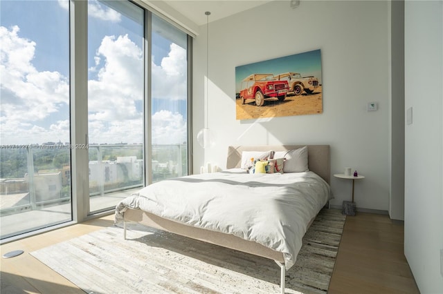 bedroom with multiple windows, expansive windows, wood-type flooring, and access to exterior