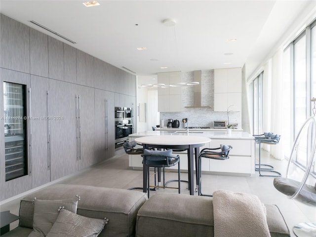 kitchen with a kitchen island with sink, wall chimney range hood, double oven, tasteful backsplash, and a breakfast bar area