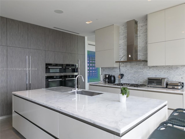 kitchen featuring backsplash, light stone counters, sink, wall chimney range hood, and stainless steel gas stovetop