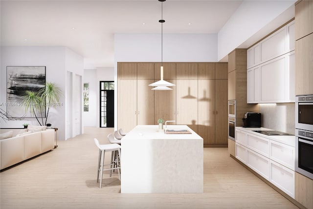 kitchen with light wood-type flooring, sink, decorative light fixtures, a center island with sink, and a breakfast bar area