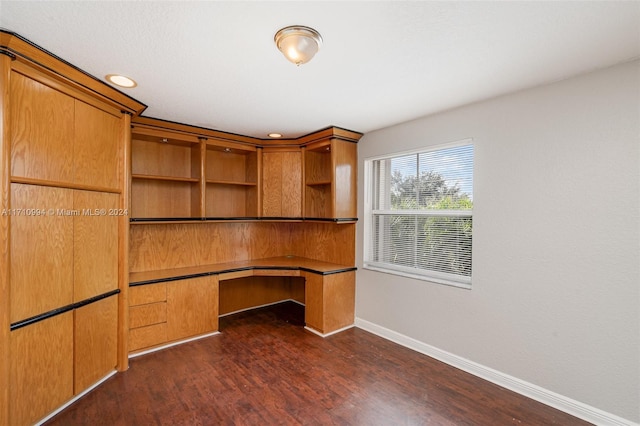 unfurnished office with dark wood-type flooring and built in desk