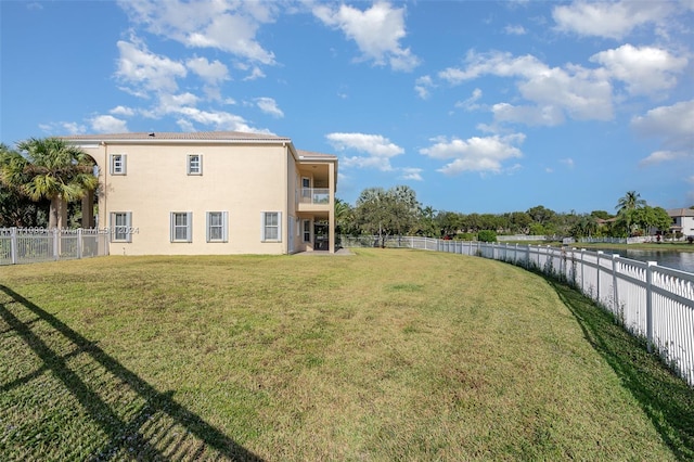 back of house featuring a lawn, a water view, and a balcony