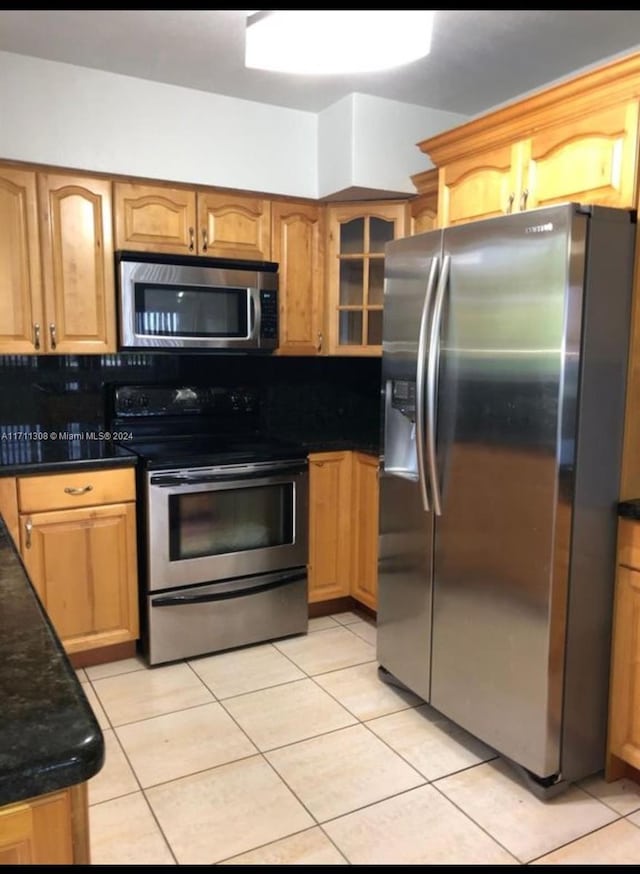 kitchen with dark stone countertops, decorative backsplash, light tile patterned flooring, and stainless steel appliances