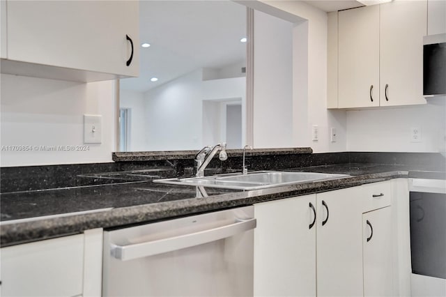 kitchen with stainless steel dishwasher, dark stone countertops, white cabinetry, and sink