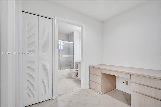 bathroom with tile patterned flooring, toilet, and combined bath / shower with glass door