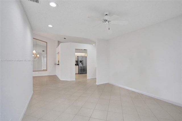 tiled spare room featuring ceiling fan with notable chandelier