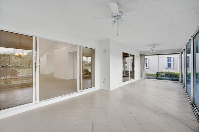 unfurnished sunroom featuring ceiling fan with notable chandelier and a wealth of natural light