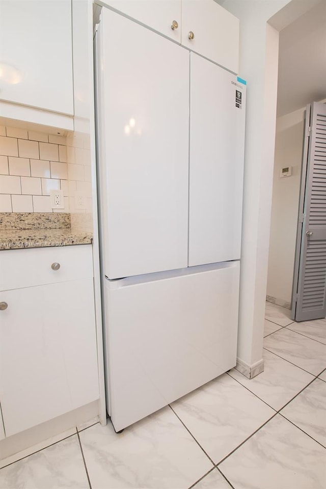 interior space featuring white cabinets, decorative backsplash, white fridge, and light stone countertops