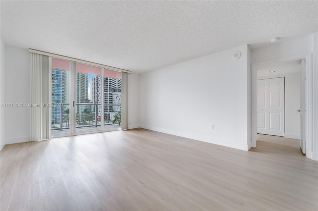 empty room with floor to ceiling windows, light hardwood / wood-style floors, and a textured ceiling