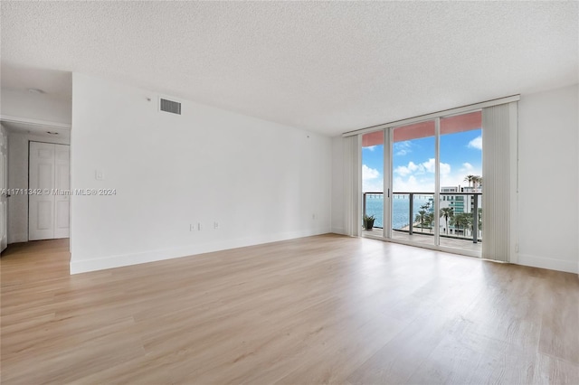 spare room with expansive windows, a water view, a textured ceiling, and light wood-type flooring