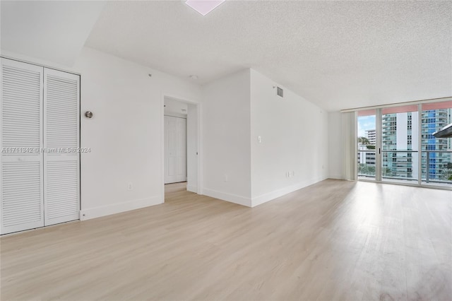 unfurnished room featuring a textured ceiling, light wood-type flooring, and a wall of windows