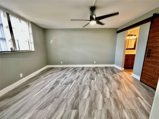 unfurnished bedroom featuring a barn door, light wood-type flooring, connected bathroom, and ceiling fan