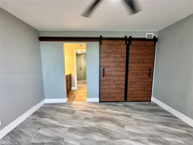 unfurnished bedroom featuring connected bathroom, a closet, ceiling fan, and a barn door