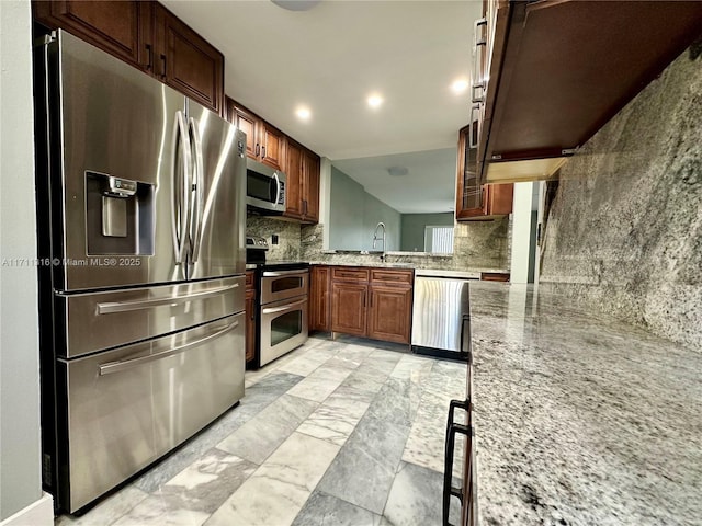 kitchen with sink, light stone counters, kitchen peninsula, stainless steel appliances, and backsplash