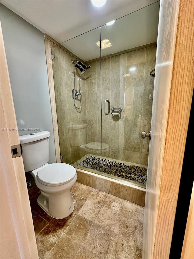 bathroom featuring a shower with door and toilet