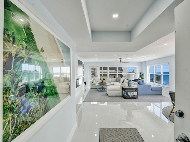 tiled living room with a tray ceiling and ceiling fan