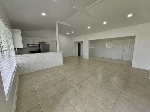 interior space featuring kitchen peninsula, appliances with stainless steel finishes, sink, white cabinetry, and lofted ceiling