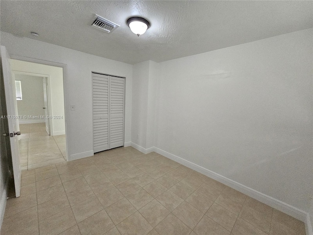 unfurnished bedroom featuring a closet, light tile patterned floors, and a textured ceiling