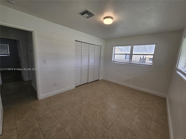 unfurnished bedroom with a closet, light tile patterned floors, and a textured ceiling