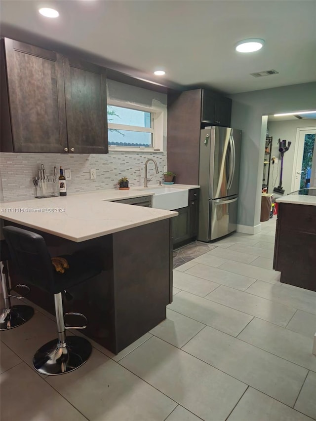 kitchen featuring sink, kitchen peninsula, stainless steel fridge, a kitchen bar, and decorative backsplash