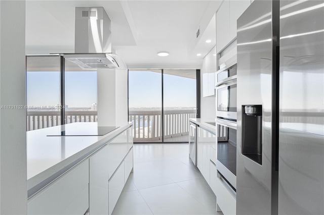 kitchen featuring island exhaust hood, expansive windows, stainless steel appliances, white cabinetry, and light tile patterned flooring