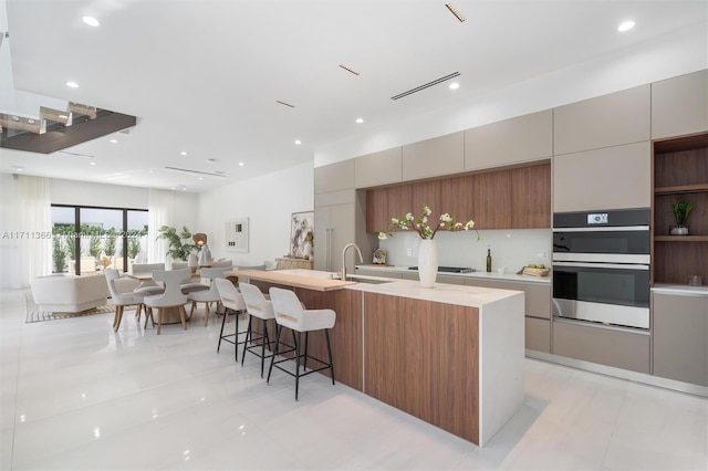 kitchen featuring sink, gas stovetop, double oven, a breakfast bar area, and light tile patterned floors