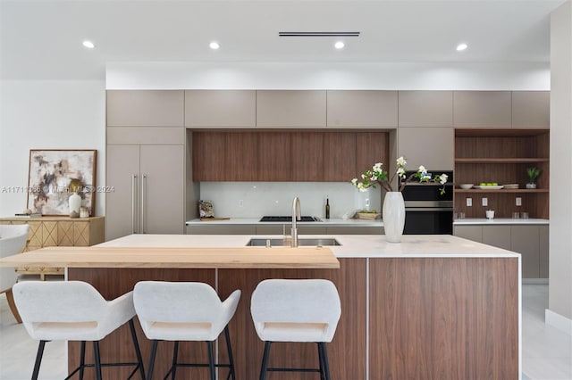 kitchen with a breakfast bar, decorative backsplash, an island with sink, and sink