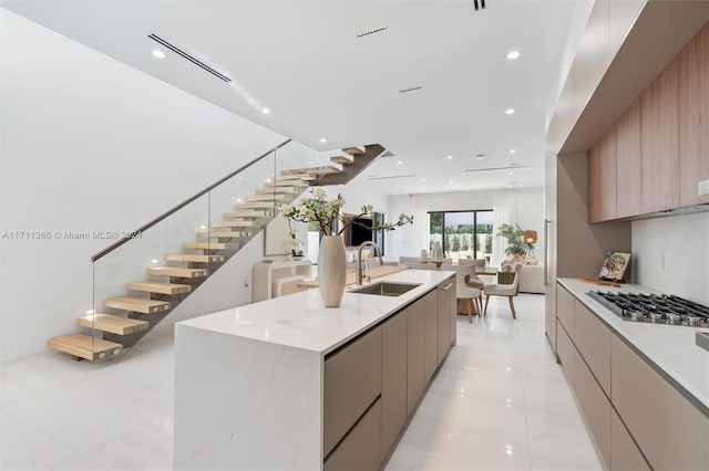 kitchen featuring light brown cabinetry, stainless steel gas cooktop, a spacious island, sink, and light tile patterned flooring