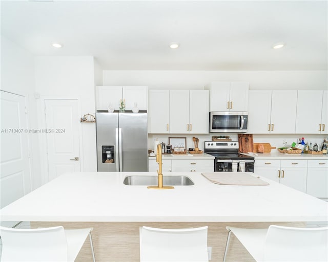 kitchen featuring white cabinetry, sink, an island with sink, a kitchen bar, and appliances with stainless steel finishes