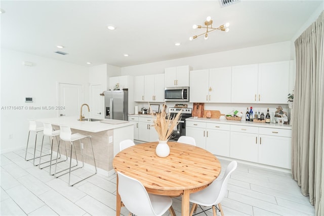 kitchen featuring stainless steel appliances, sink, white cabinets, a breakfast bar area, and an island with sink