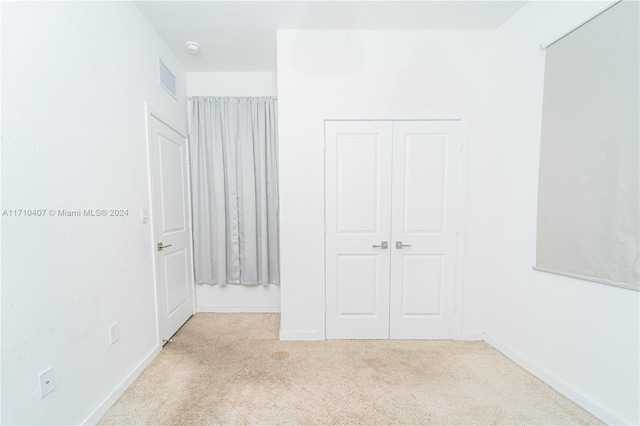 unfurnished bedroom with light colored carpet and a closet