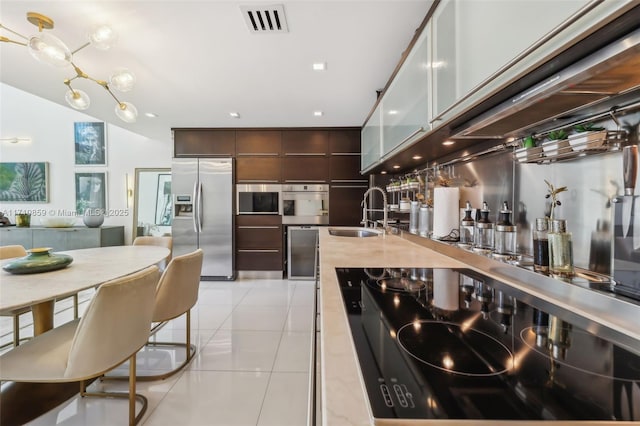 kitchen featuring dark brown cabinets, stainless steel appliances, light tile patterned floors, and sink