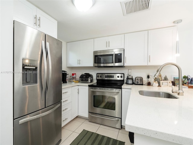 kitchen with sink, light stone countertops, light tile patterned floors, appliances with stainless steel finishes, and white cabinetry