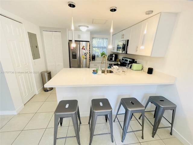 kitchen with kitchen peninsula, appliances with stainless steel finishes, a breakfast bar, decorative light fixtures, and white cabinetry