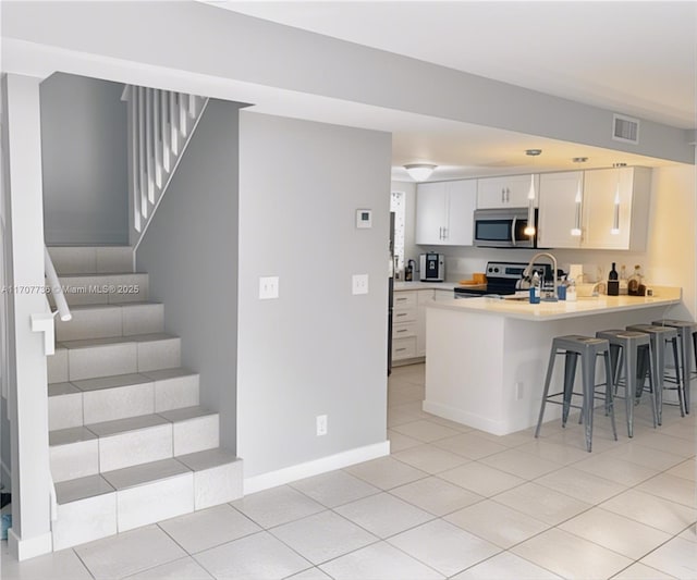 kitchen with a breakfast bar, white cabinets, light tile patterned floors, appliances with stainless steel finishes, and kitchen peninsula