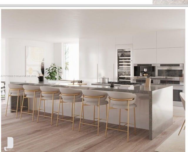 kitchen with white cabinets, a kitchen bar, light wood-type flooring, and appliances with stainless steel finishes