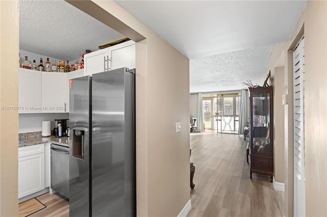 kitchen with white cabinetry, stainless steel appliances, light hardwood / wood-style flooring, dark stone countertops, and a textured ceiling