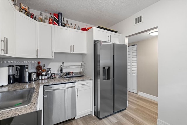 kitchen featuring appliances with stainless steel finishes, a textured ceiling, sink, light hardwood / wood-style floors, and white cabinetry