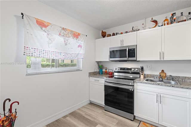 kitchen with sink, a textured ceiling, light hardwood / wood-style floors, white cabinetry, and stainless steel appliances