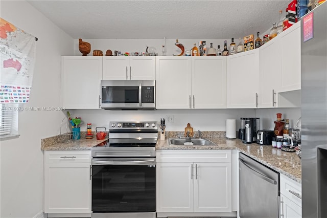 kitchen featuring light stone counters, a textured ceiling, stainless steel appliances, sink, and white cabinets