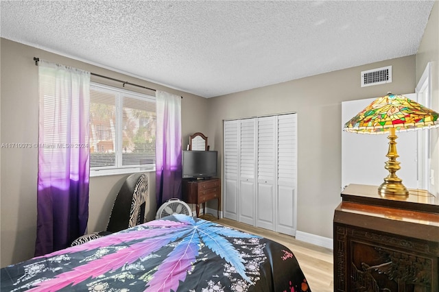 bedroom with a textured ceiling, light wood-type flooring, and a closet