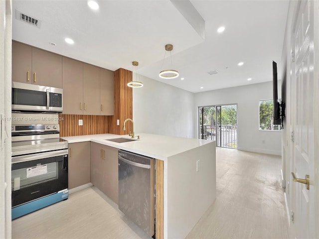 kitchen featuring sink, light hardwood / wood-style flooring, appliances with stainless steel finishes, decorative light fixtures, and kitchen peninsula