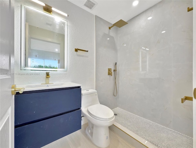 bathroom with a tile shower, vanity, and toilet