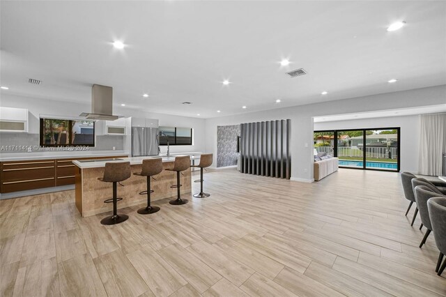 kitchen featuring stainless steel fridge, a breakfast bar, a kitchen island with sink, island range hood, and light wood-type flooring