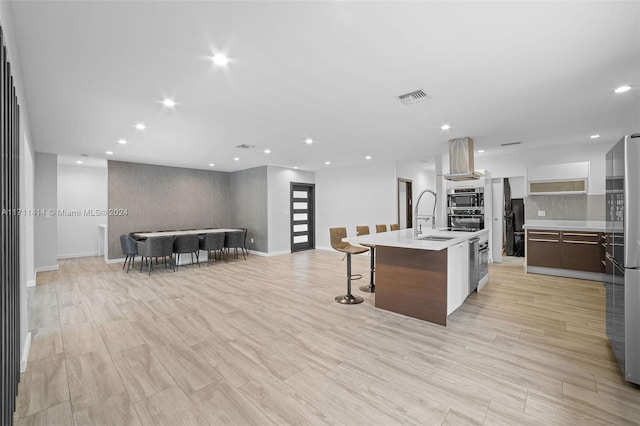 kitchen with sink, stainless steel fridge, island exhaust hood, a large island with sink, and light wood-type flooring