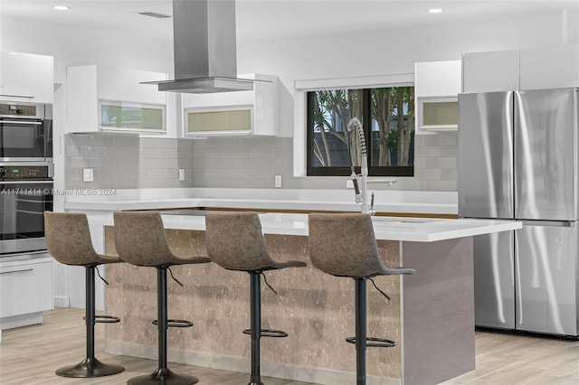 kitchen with a kitchen bar, a center island, island exhaust hood, stainless steel appliances, and white cabinets